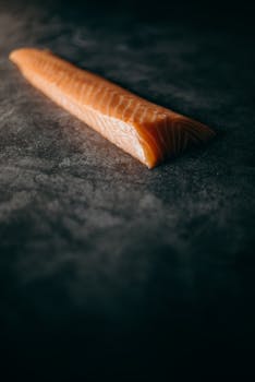 A raw salmon fillet placed on a dark textured surface in a low-light setting.