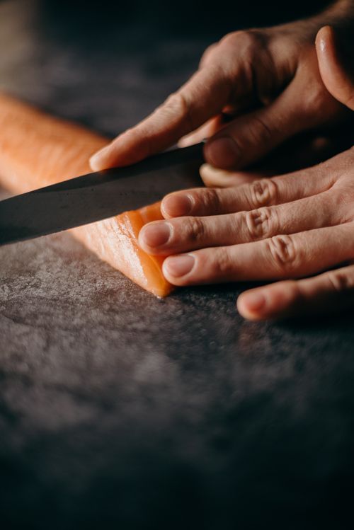 Free Close-up of hands skillfully slicing fresh salmon fillet for delicious Japanese cuisine. Stock Photo