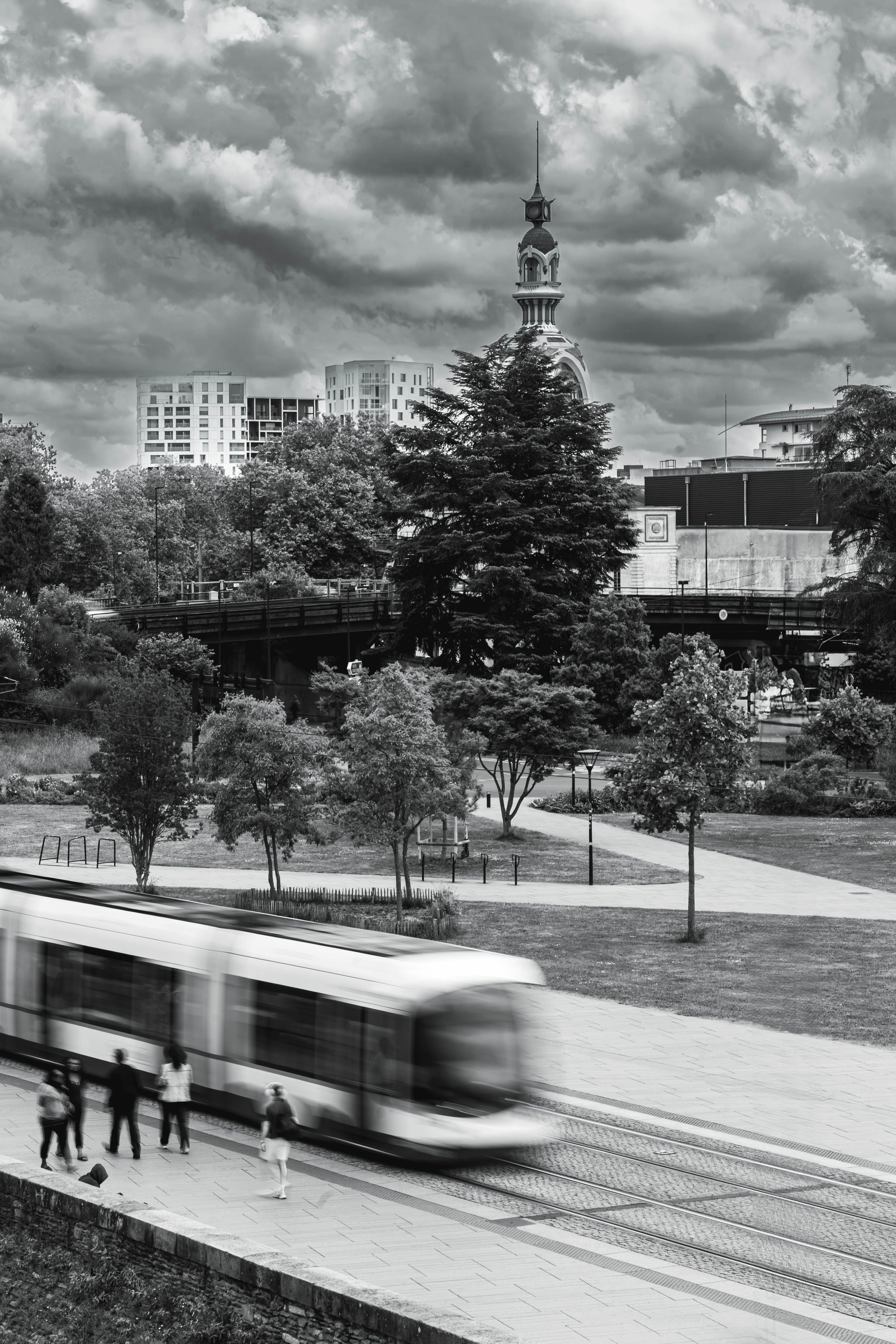 Dramatic black and white image of a tram in motion with city skyline and church in Nantes.