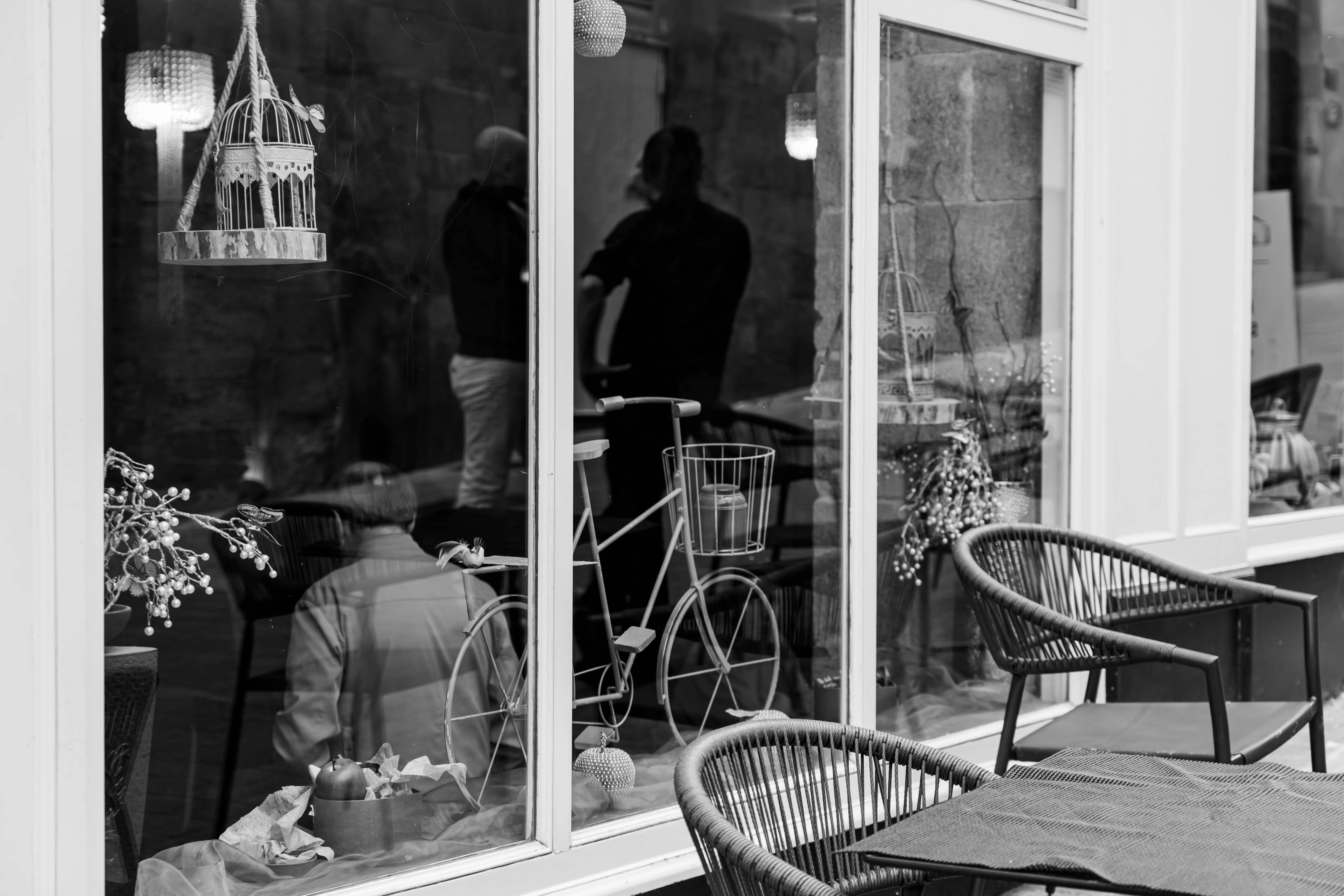 Monochrome street scene reflecting a vintage bike and passerby in shop window.