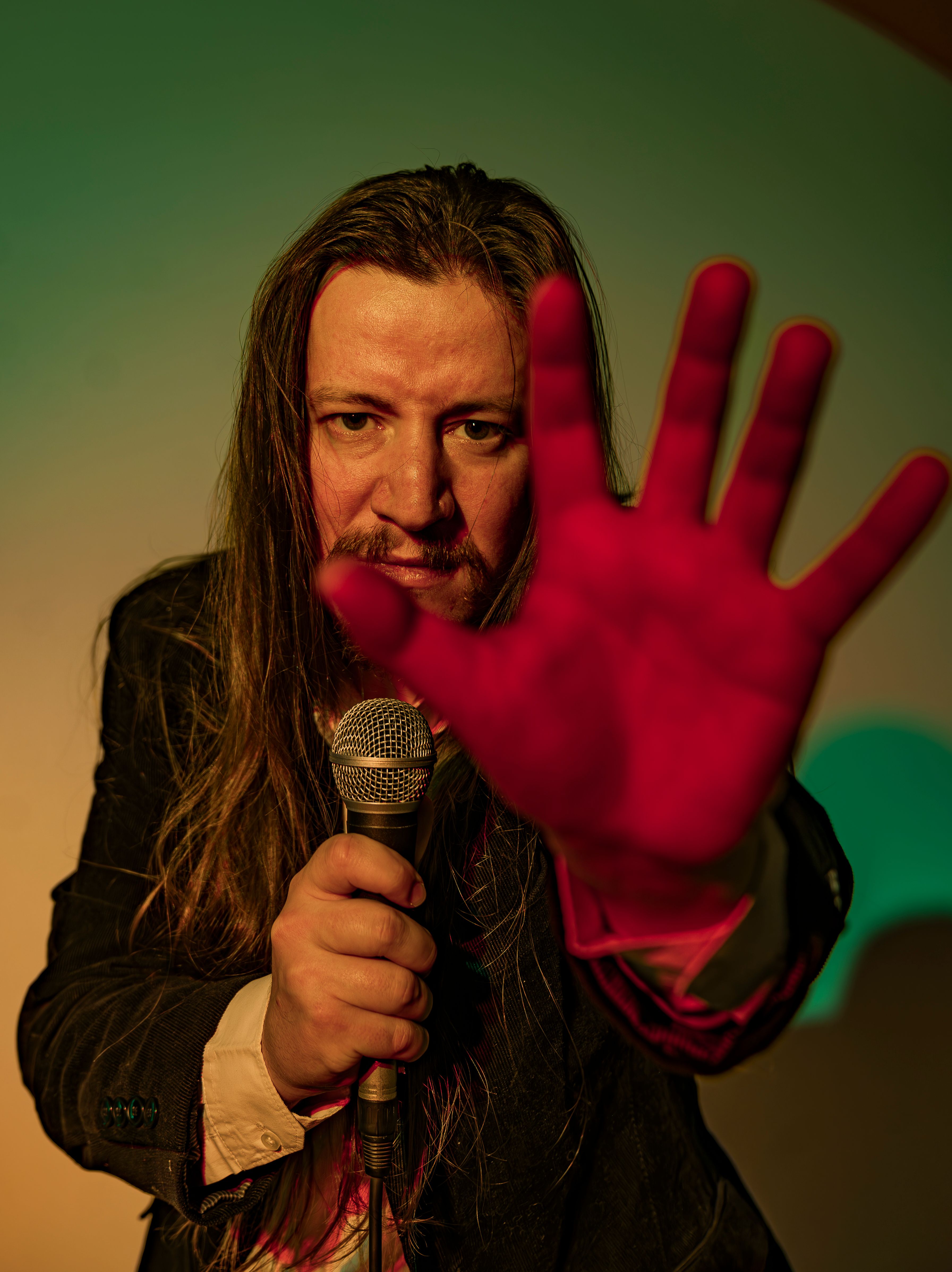 Dramatic portrait of a man with long hair holding a microphone, emphasizing vibrant colors.