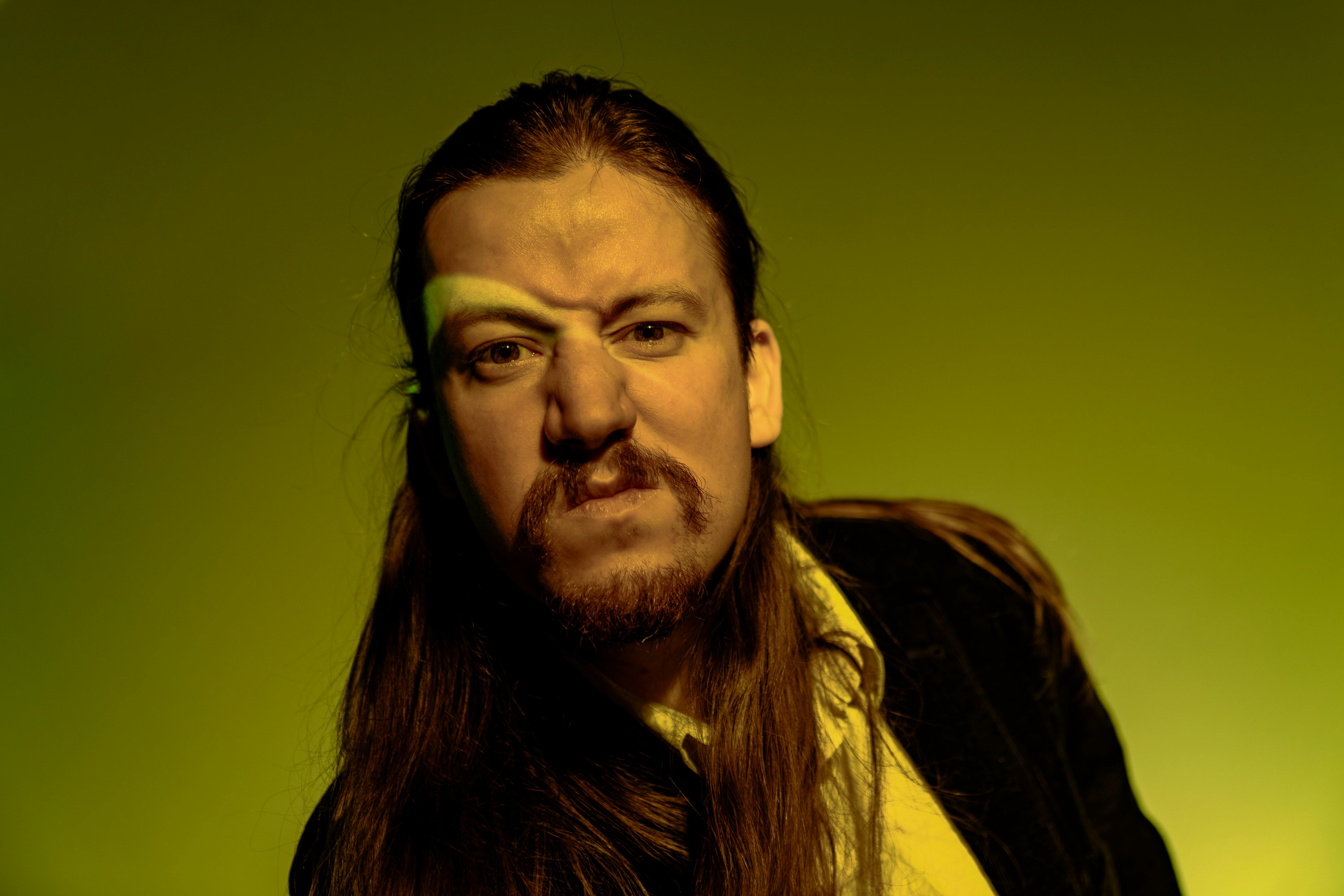 Dramatic portrait of a man with long hair and beard under intense yellow lighting.