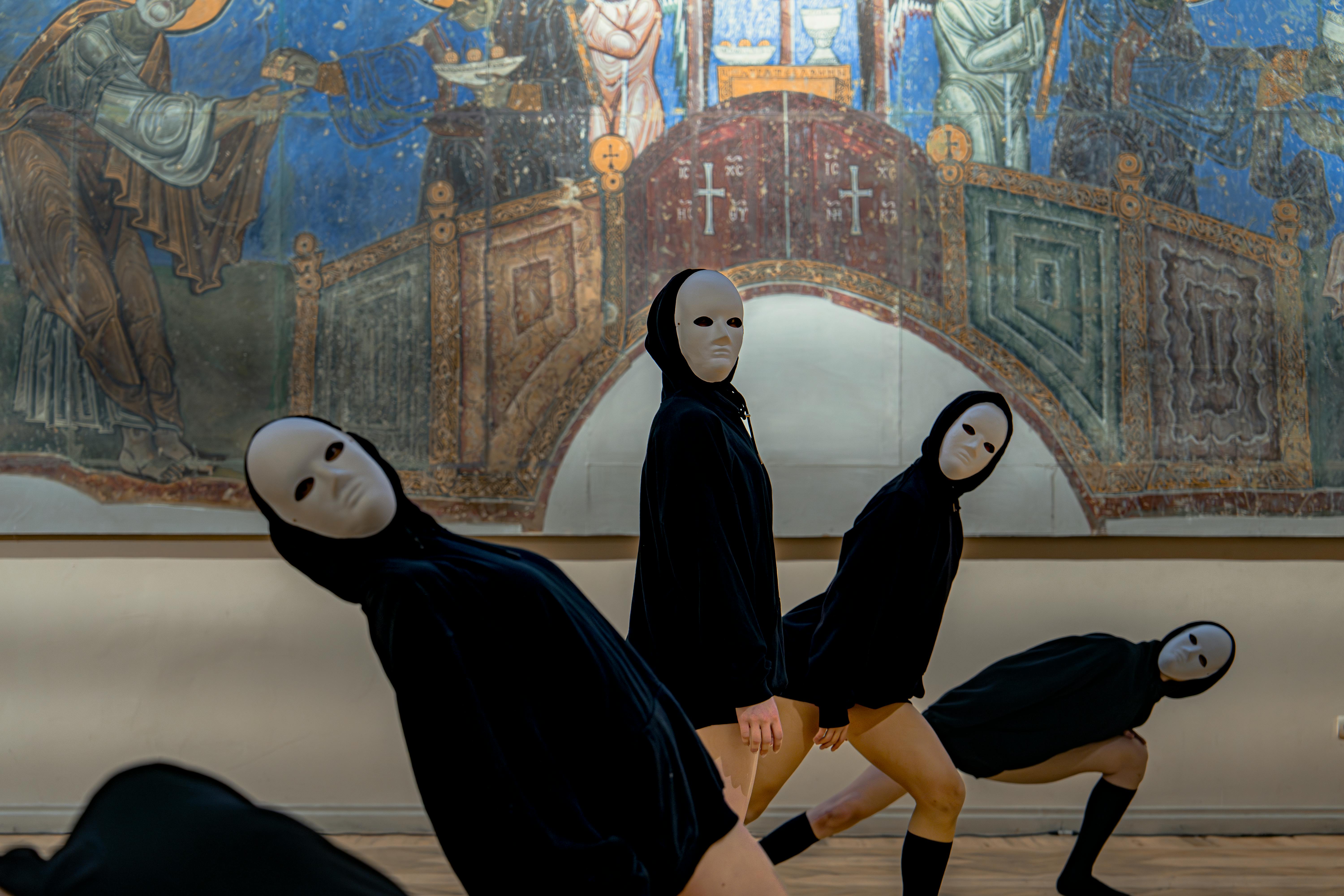 Kostenlos Maskierte Personen führen vor dem Hintergrund religiöser Kunst ausdrucksstarke Tänze auf und schaffen so eine geheimnisvolle Atmosphäre. Stock-Foto