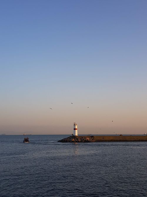 Free Peaceful evening view of a lighthouse on Istanbul seafront with calm waters and a soft sunset sky. Stock Photo