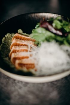 Close-up of fresh salmon sashimi served with leafy greens on a plate.