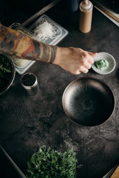 Tattooed chef prepares fresh greens and ingredients in a moody kitchen setup.