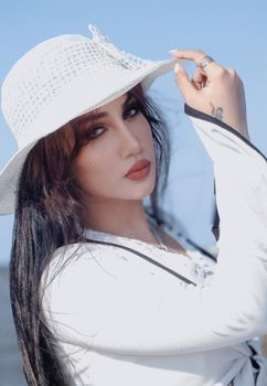 Elegant young woman wearing a white hat and posing outdoors on a sunny day.