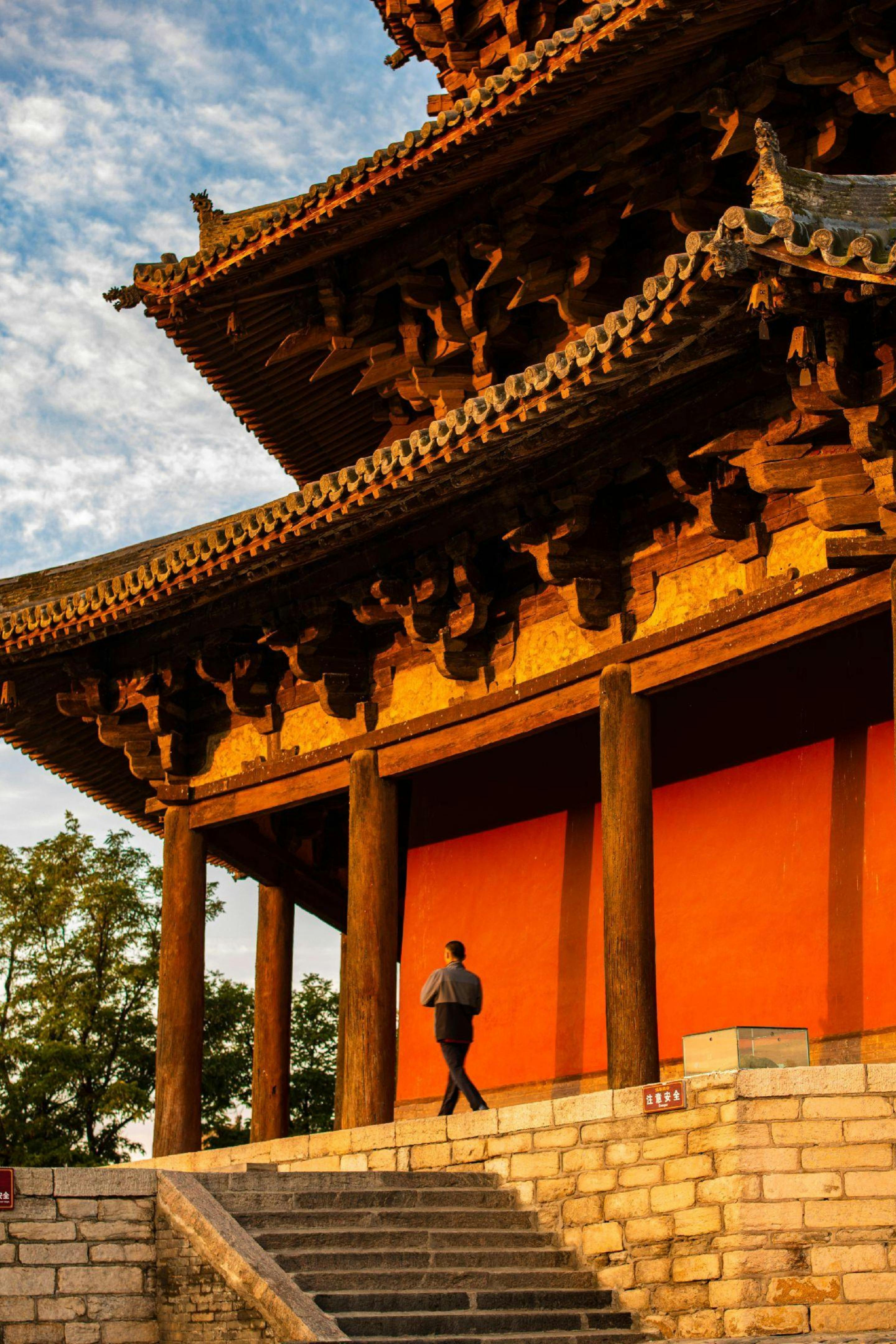 A man walks by an ancient wooden pagoda bathed in sunset light in Shaanxi, China.