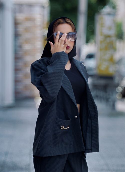 Free Stylish woman in a black outfit and sunglasses posing confidently on a city street. Stock Photo