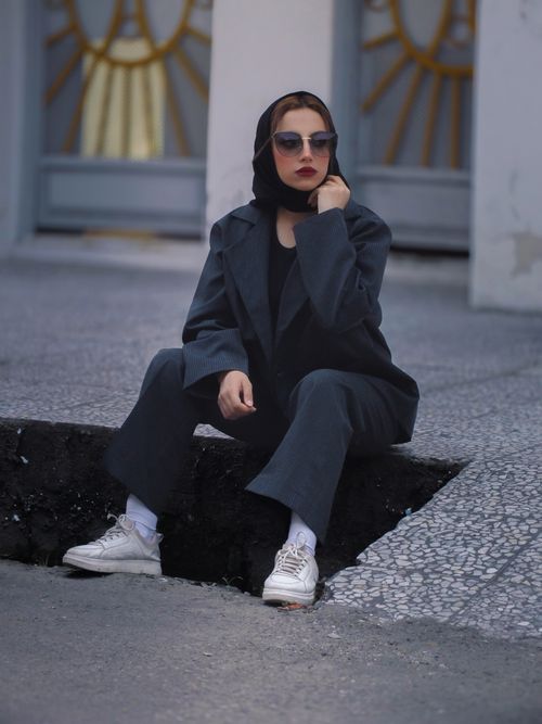 Free A stylish woman wearing sunglasses and a dark suit sitting outdoors, exuding a modern vibe. Stock Photo