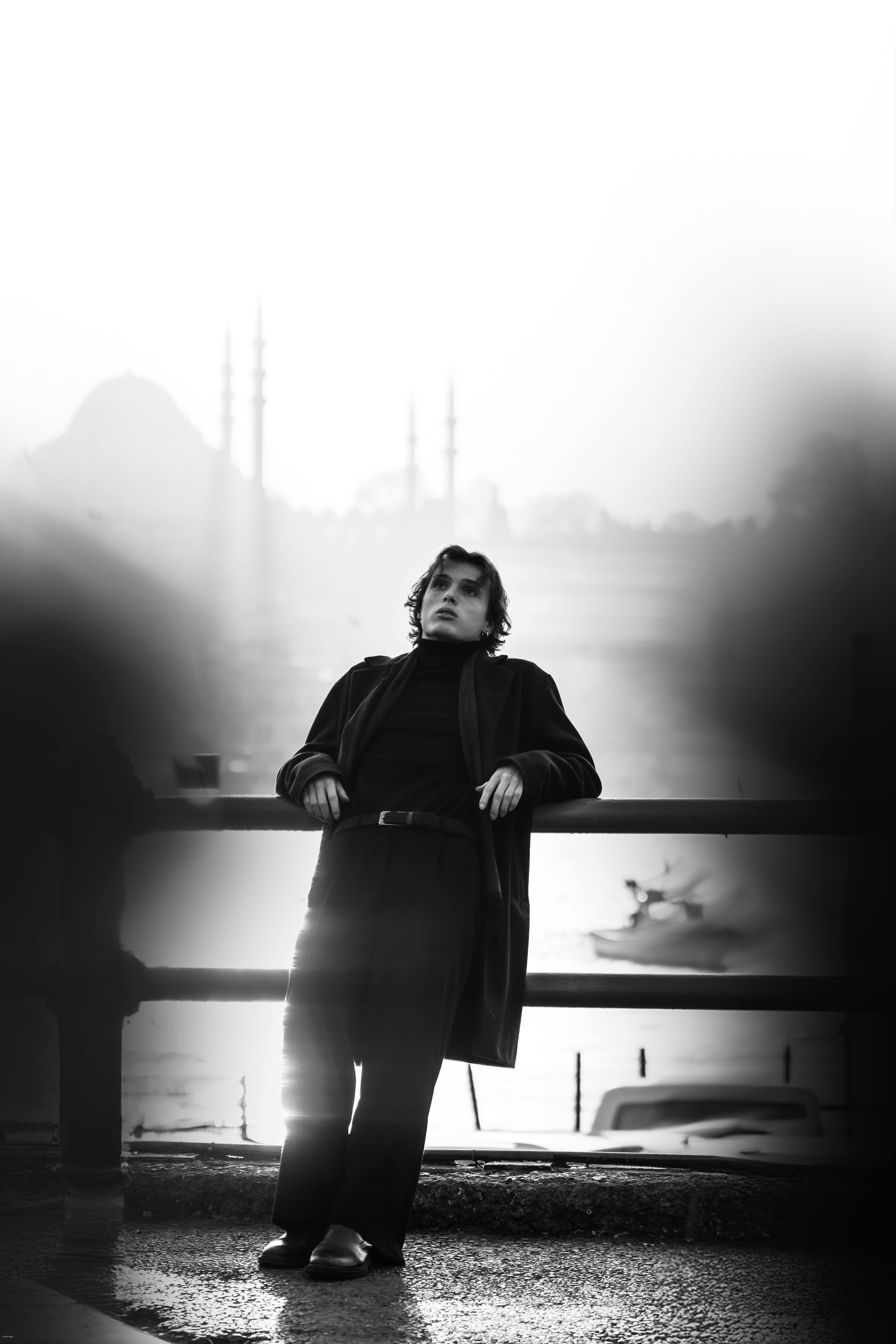 Expressive black and white portrait of a man leaning on a bridge railing in Istanbul at night.