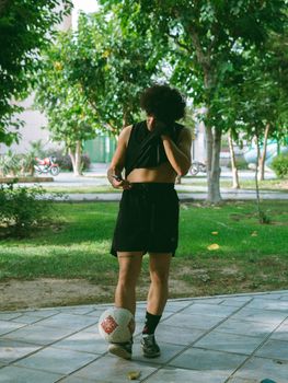 Young adult practicing soccer skills in a park, balancing a ball on foot. Green environment under bright daylight.
