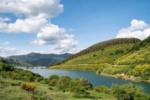 Free A picturesque view of a river surrounded by green hills under a bright blue sky. Stock Photo