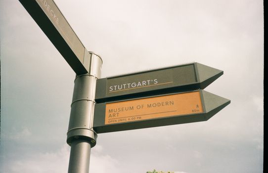Signpost directing to Stuttgart's Museum of Modern Art under an overcast sky.