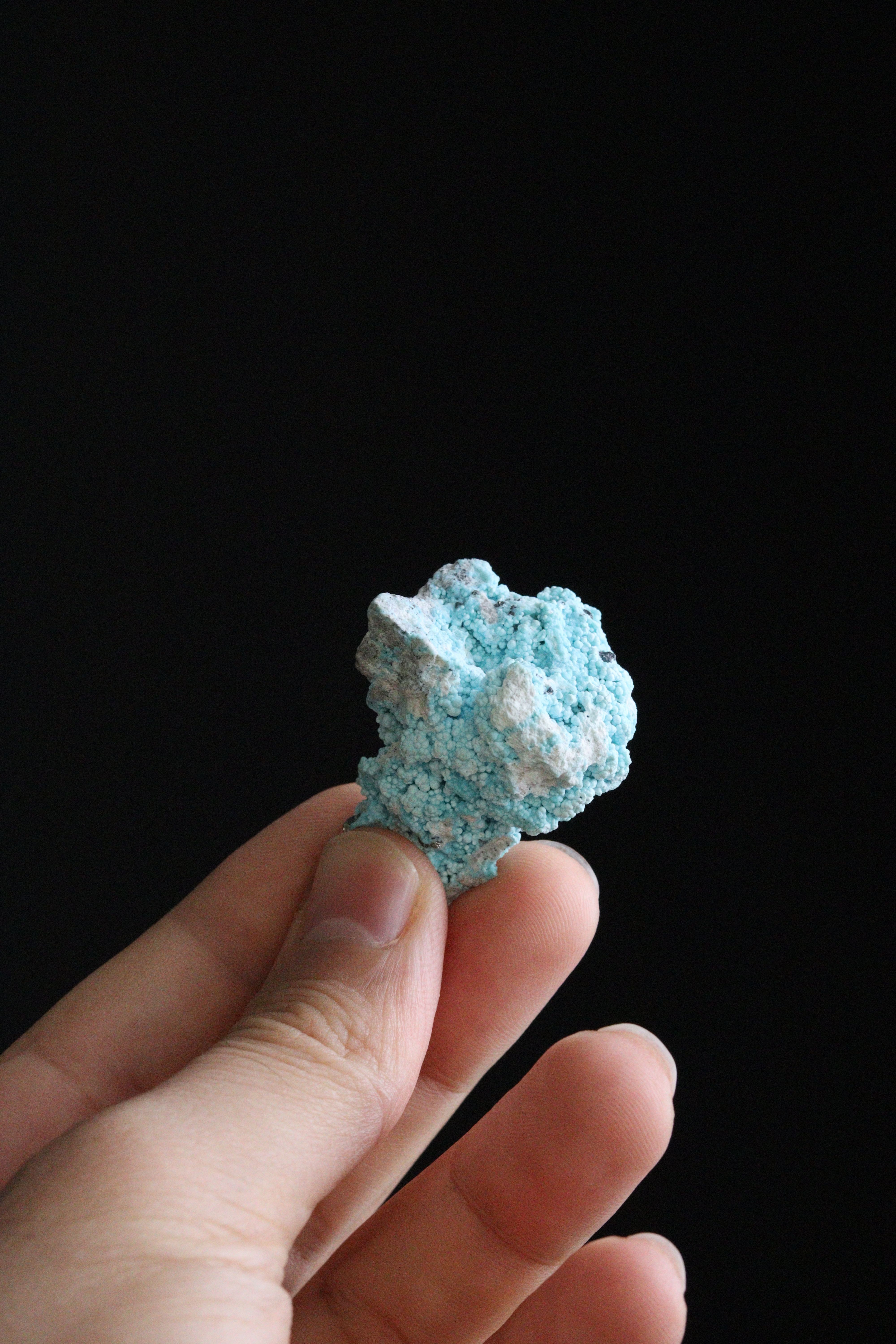 A blue mineral rock held by a hand against a dark background, showcasing its unique texture.