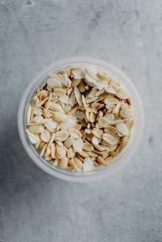 A clear bowl full of sliced almonds viewed from above on a textured surface.