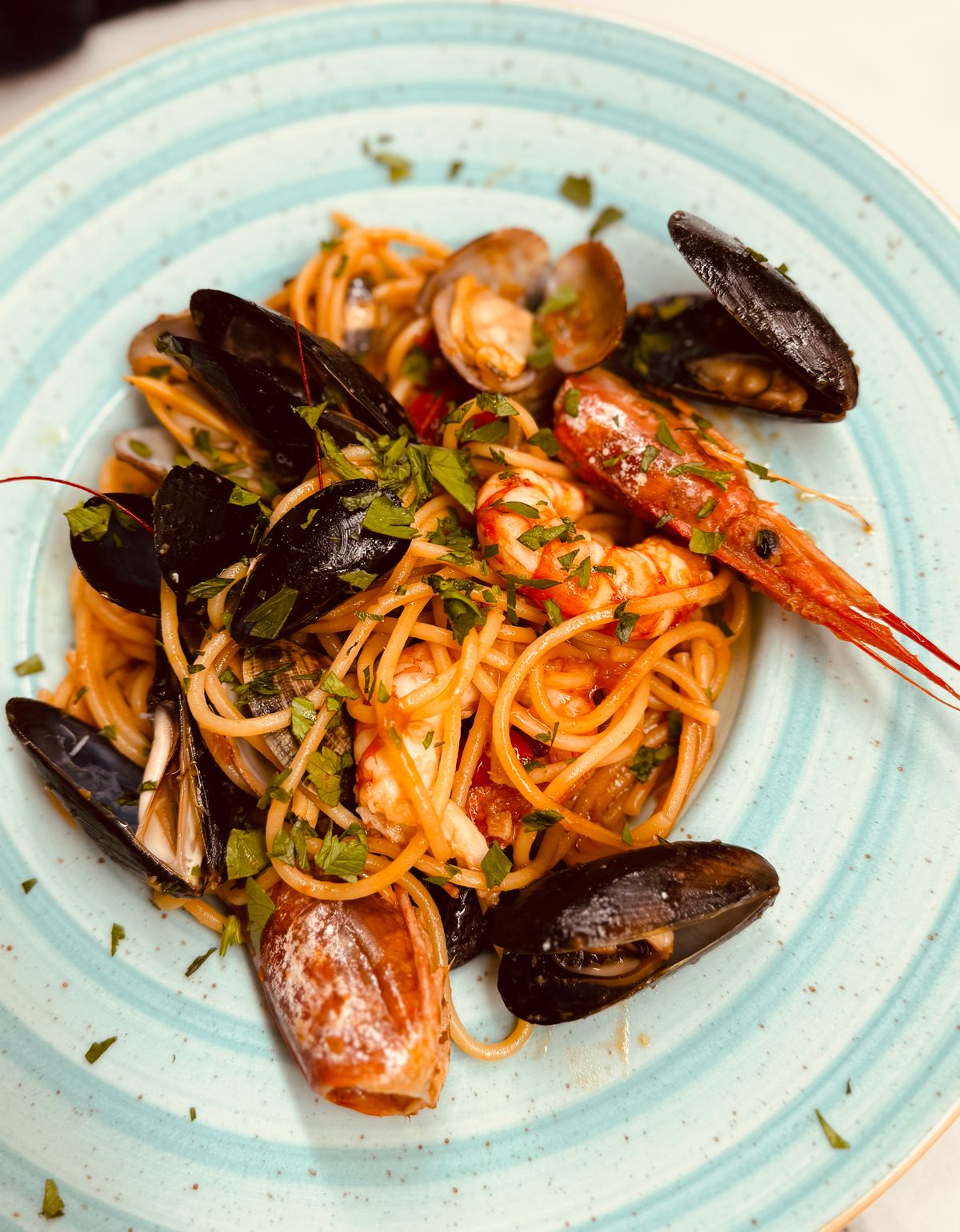 Spaghetti with mussels and shrimp on a light blue striped plate