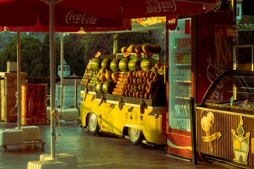 Colorful fruit stand selling watermelon and oranges at sunset outside a market.