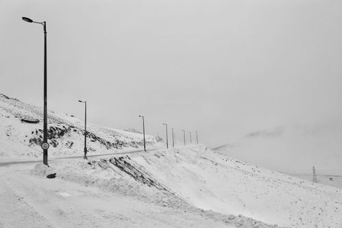 Free Serene snowy mountain road with street lamps and snow-covered landscape under overcast sky. Stock Photo