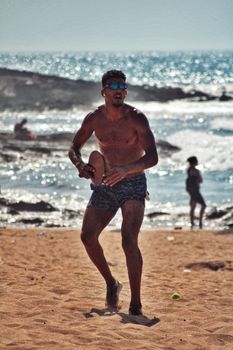 Athletic man playing paddleball on a sandy beach with an ocean view. Ideal for summer lifestyle themes.
