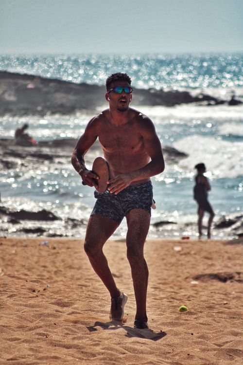 Free Athletic man playing paddleball on a sandy beach with an ocean view. Ideal for summer lifestyle themes. Stock Photo