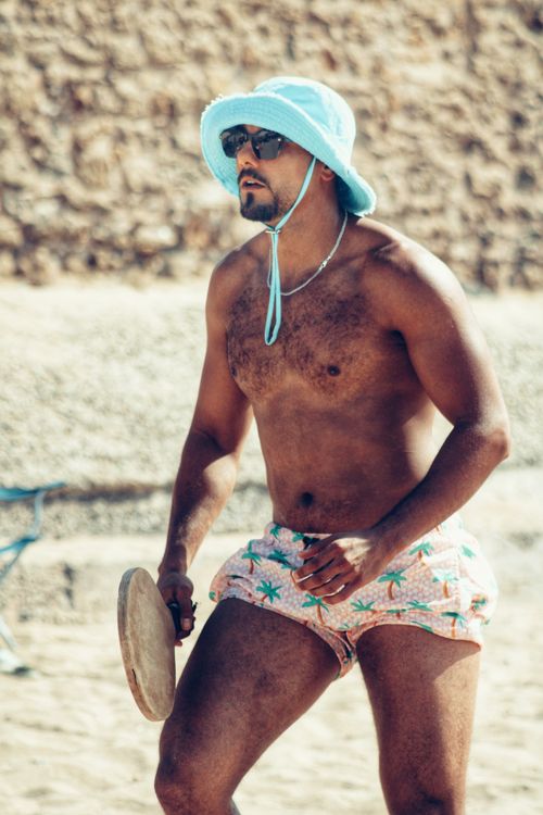 Free A man in sunglasses and a hat plays paddle ball on a sandy beach, enjoying the summer sun. Stock Photo