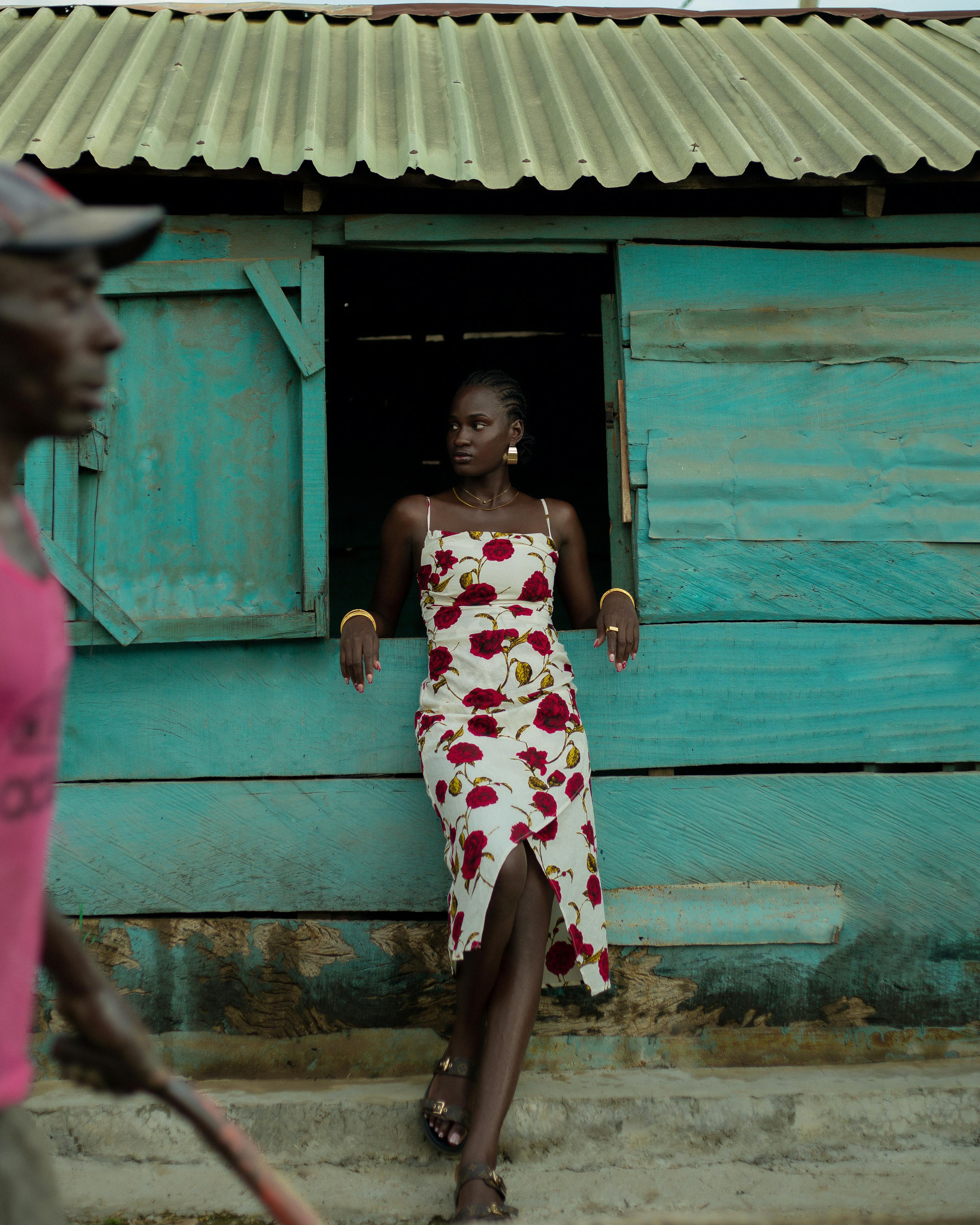 ฟรี หญิงสาวแต่งตัวมีสไตล์ในชุดเดรสลายดอกไม้พิงกำแพงสีเขียวอมฟ้าสไตล์ชนบทในเมืองอิโลริน ประเทศไนจีเรีย คลังภาพถ่าย