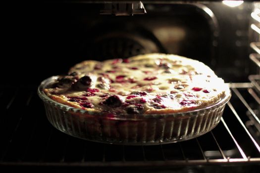 A freshly baked cherry clafoutis in a glass dish inside an oven, capturing the essence of homemade desserts.