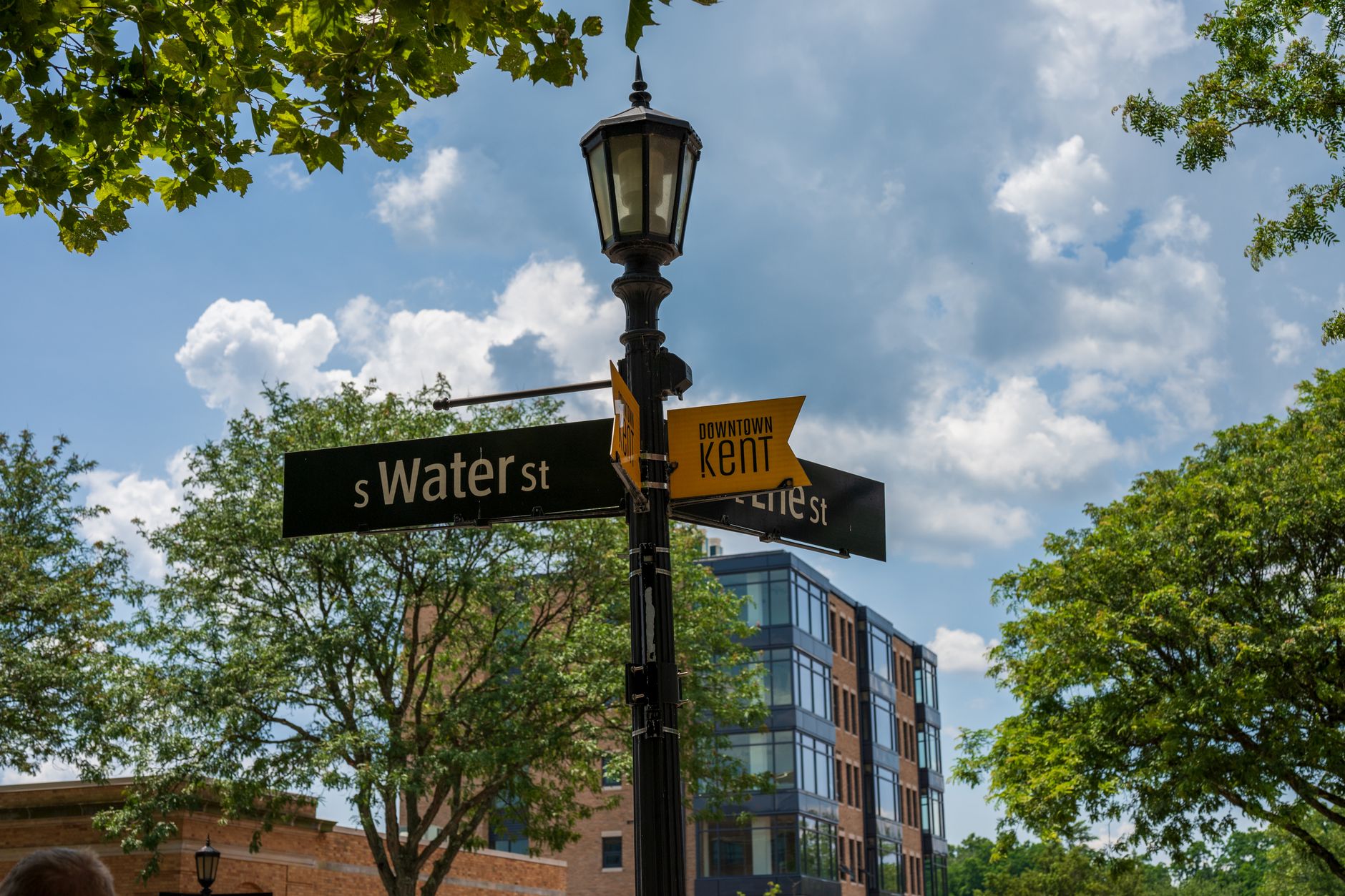 Street signs and lush trees in downtown Kent, Ohio, under a clear blue sky.