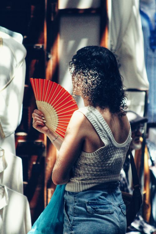 Free Back of a woman holding a red fan in a market setting, lit by beams of sunlight. Stock Photo