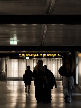 Silhouettes of travelers walking towards gates in an airport terminal corridor.