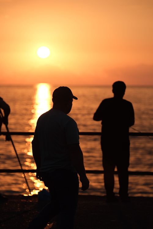 Free Silhouettes of people by the sea at sunset, capturing a serene and warm moment. Stock Photo
