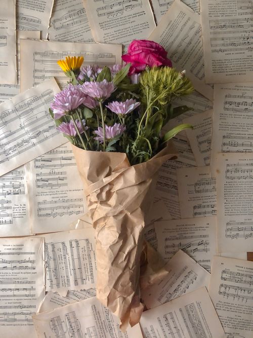 Free Floral bouquet wrapped in paper on a bed of vintage sheet music, exuding a classic aesthetic. Stock Photo