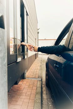 A friendly drive-thru interaction with hands exchanging items at a fast-food window.
