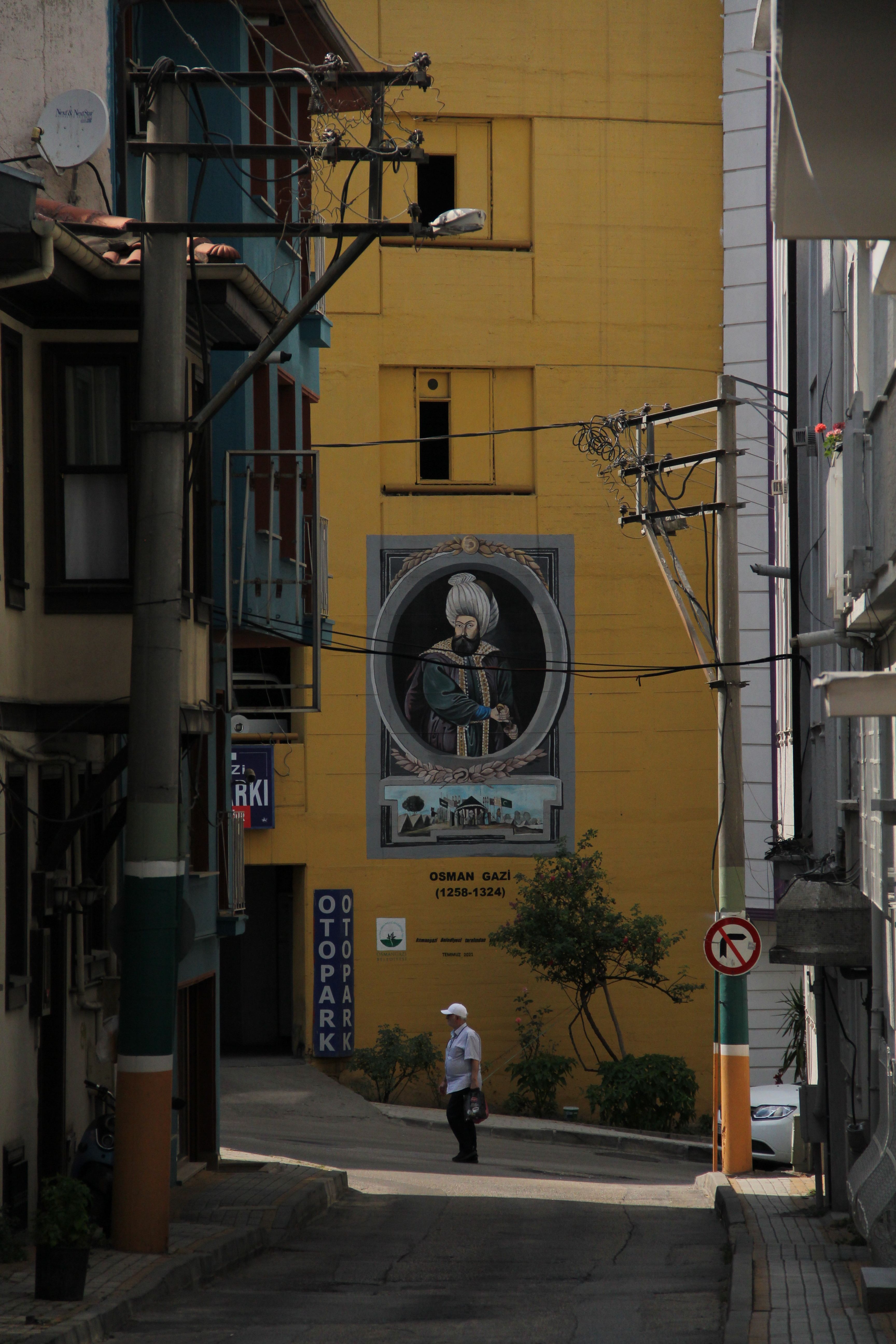 A narrow urban alley featuring a prominent historical wall mural of Osman Gazi in Istanbul.