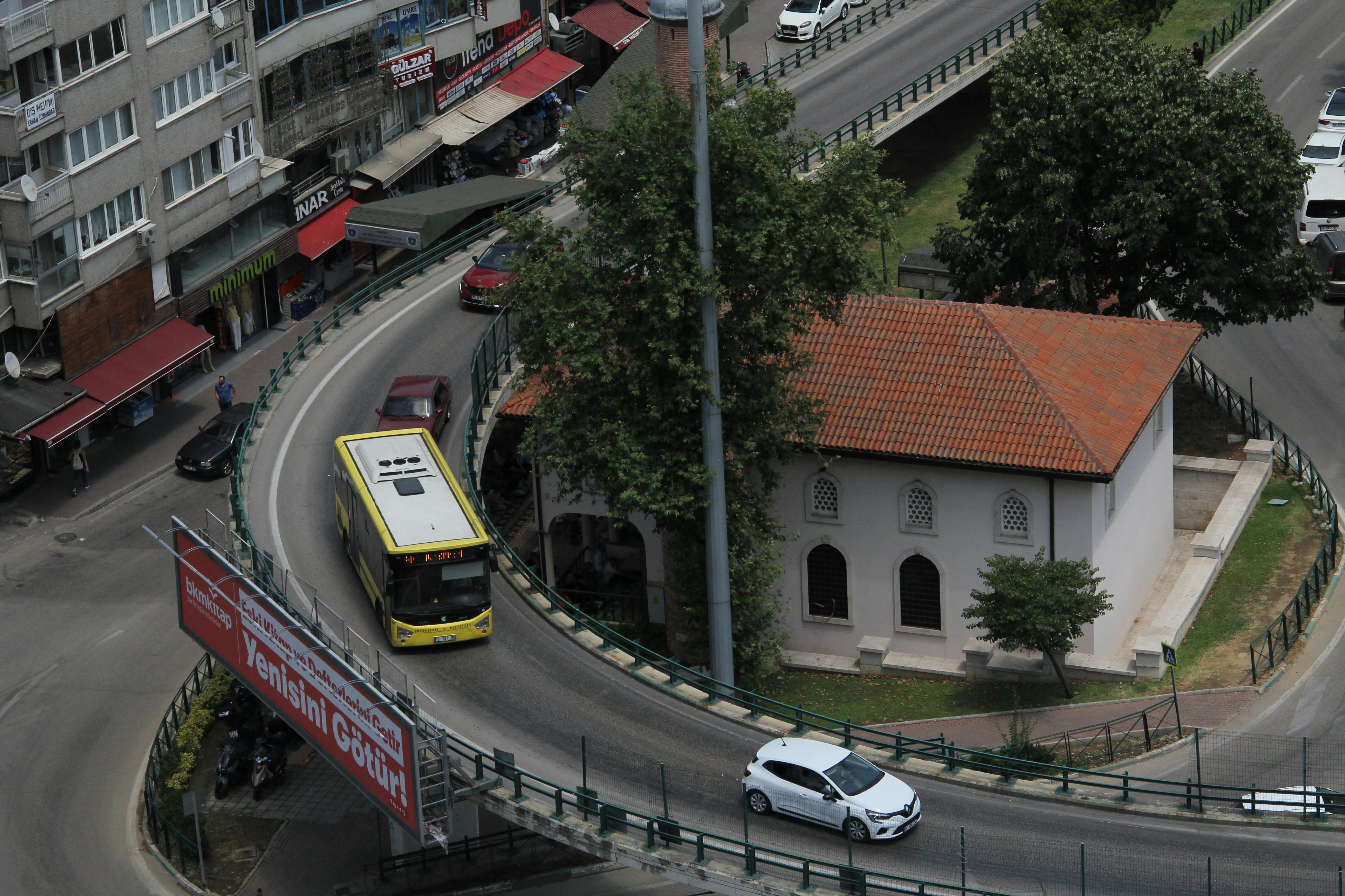 Aerial shot of a curving city road with vehicles and a traditional building in an urban setting.
