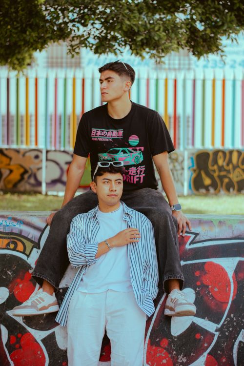 Free Two young men posing casually against vibrant graffiti wall in an urban setting. Stock Photo
