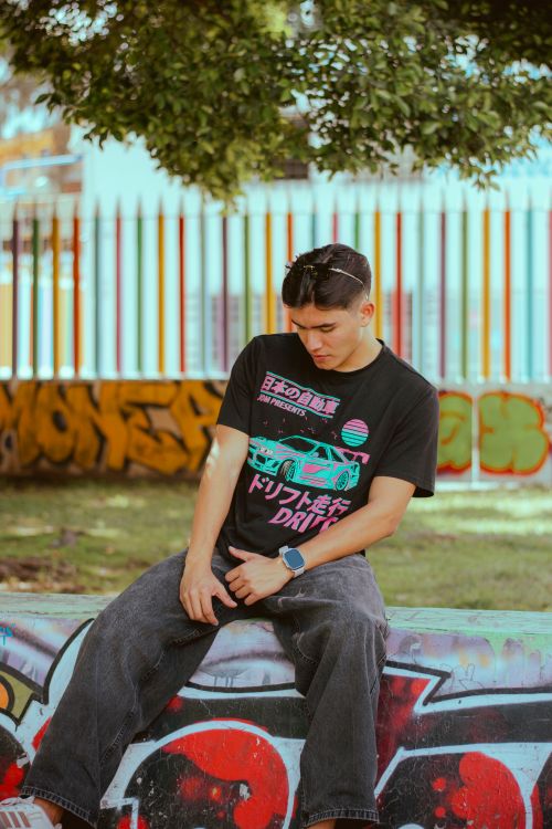 Free Casual portrait of a young man sitting in front of vibrant graffiti in an outdoor urban setting. Stock Photo