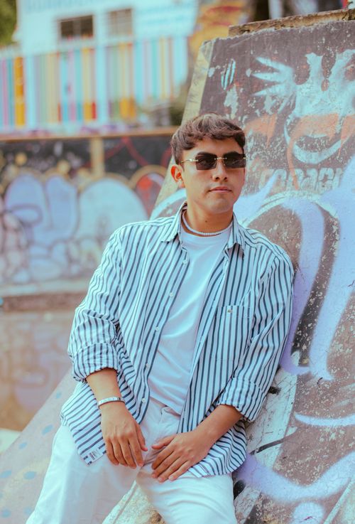 Free Young adult in striped shirt poses by vibrant graffiti in urban setting. Stock Photo