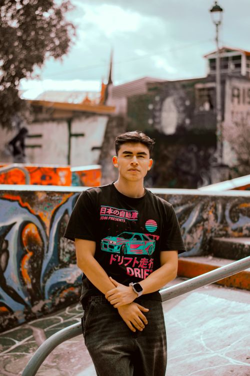 Free Young adult standing in a colorful graffiti-covered skatepark, relaxed and stylish. Stock Photo