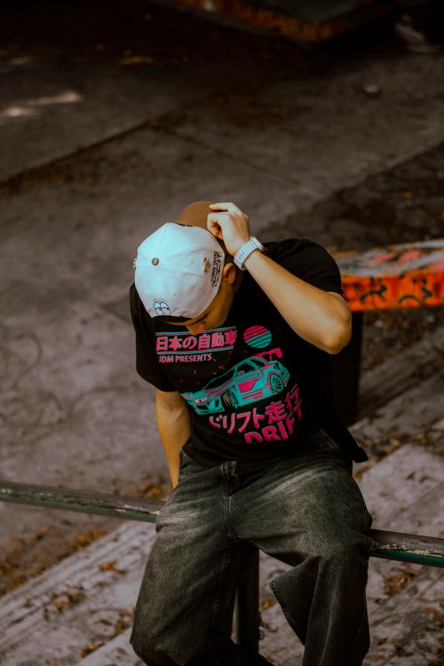 Free Street style fashion featuring a man in a graphic T-shirt and cap sitting outdoors. Stock Photo