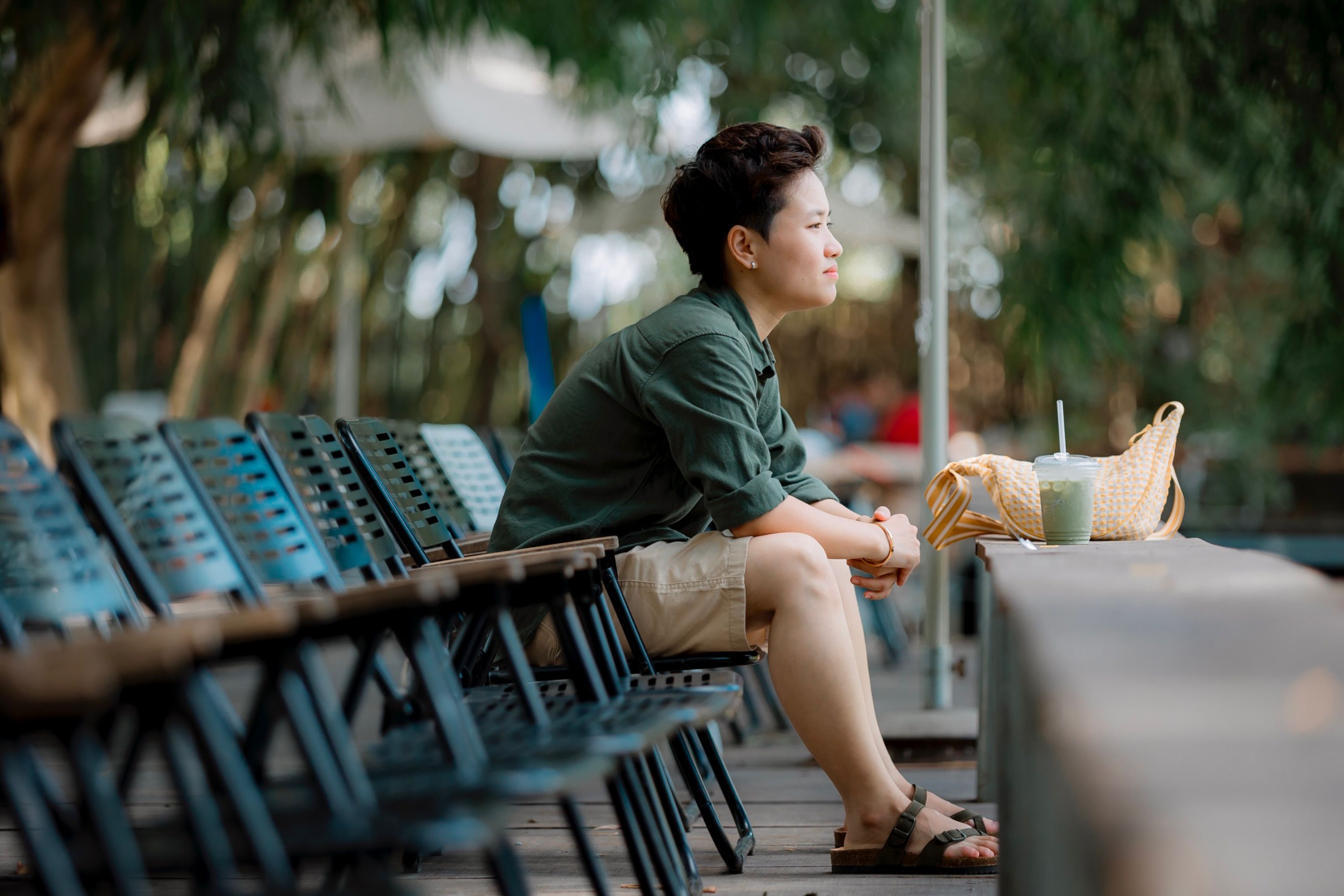 Woman in casual attire seated outdoors, enjoying iced matcha tea.