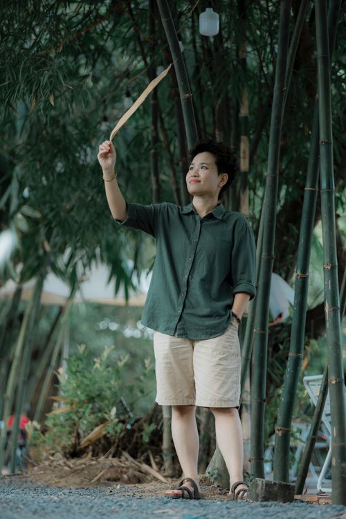 Free Adult standing outdoors holding leaf, surrounded by tall bamboo and greenery. Stock Photo