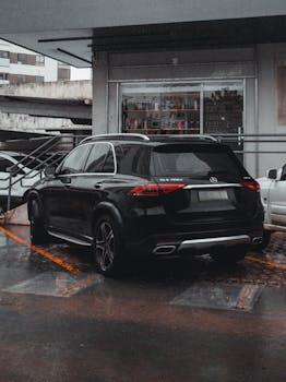 Black Mercedes SUV parked in a rainy urban setting outside a commercial building, showcasing modern design.