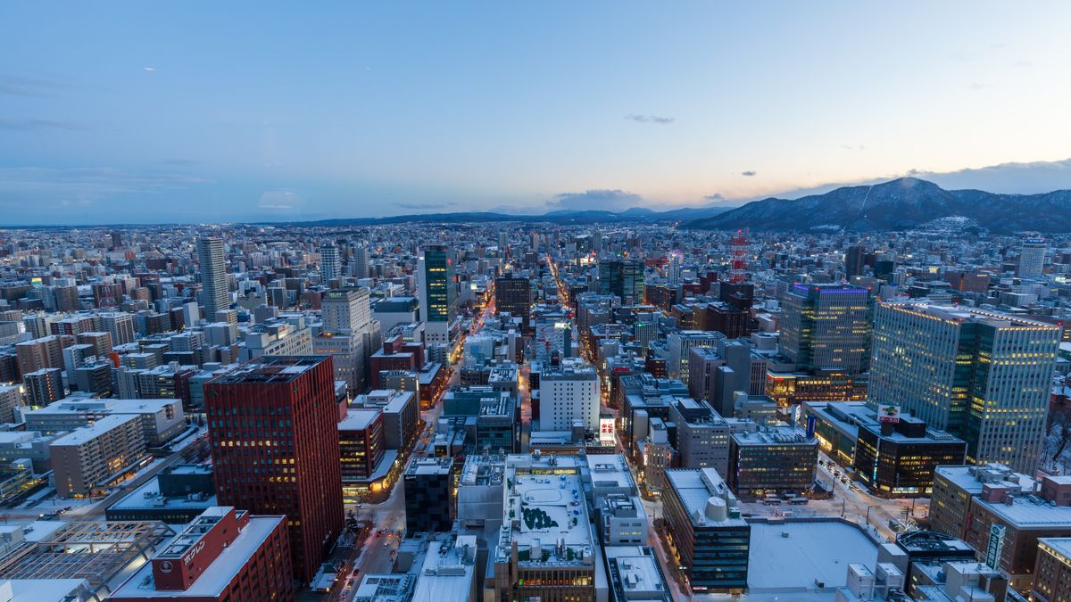 삿포로 — Captivating aerial view of Sapporo, Japan in winter at dusk with snow-covered buildings and distant mountains.