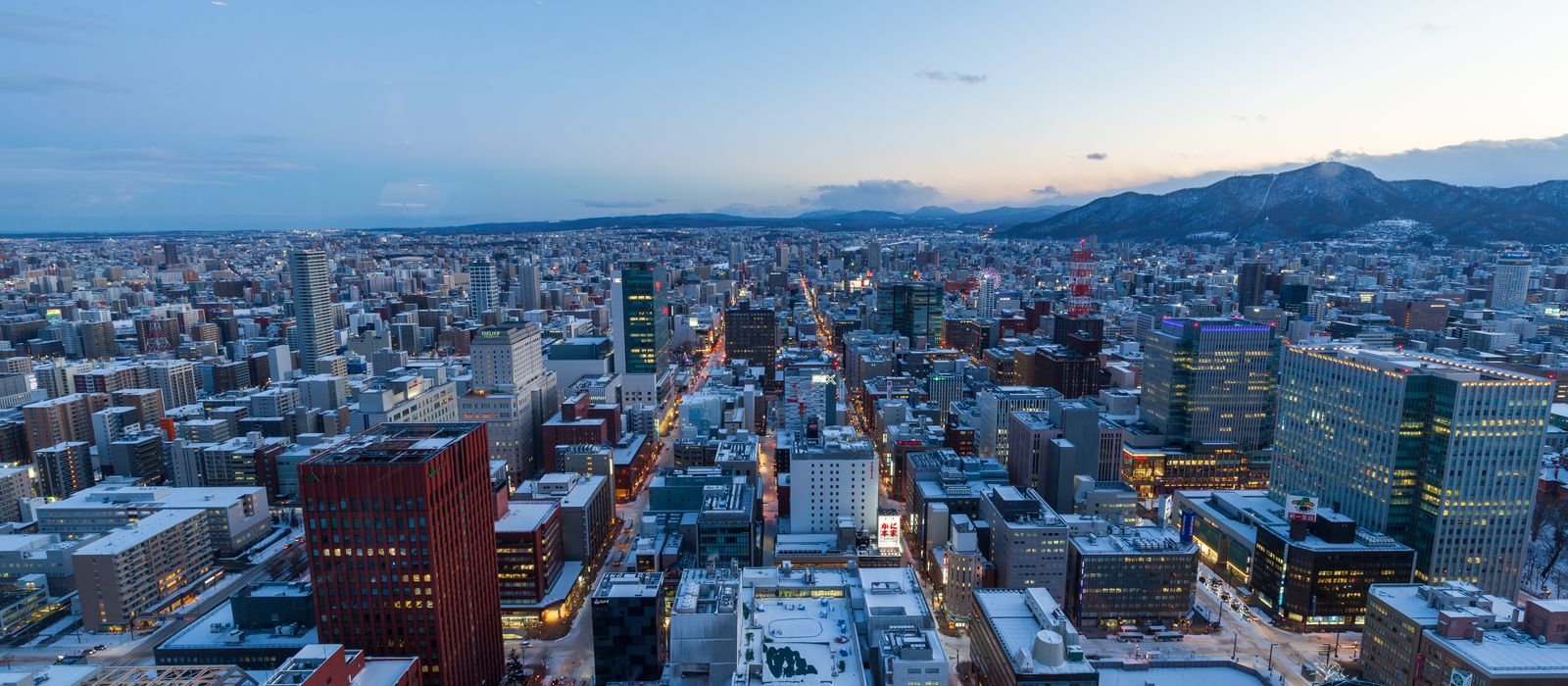 Captivating aerial view of Sapporo, Japan in winter at dusk with snow-covered buildings and distant mountains. — flights from Tokyo to Sapporo