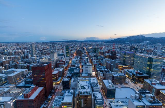 Captivating aerial view of Sapporo, Japan in winter at dusk with snow-covered buildings and distant mountains. — arriving in Sapporo