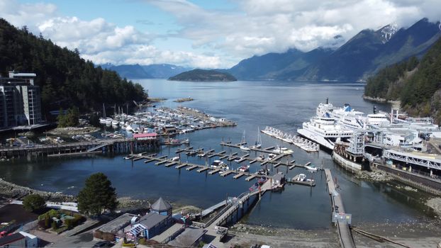 Aerial shot of a bustling harbor surrounded by majestic mountains and clear skies.