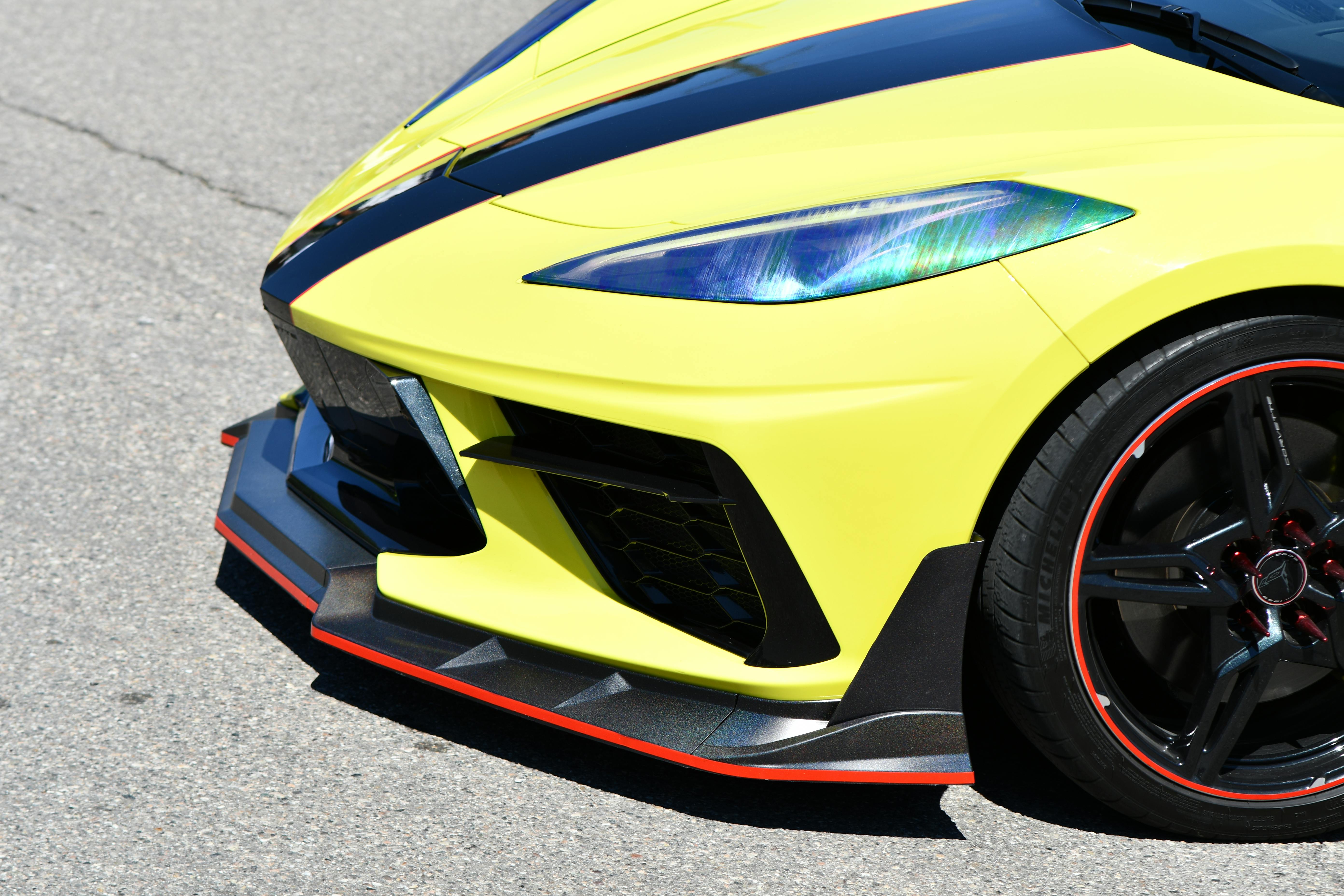 Detailed photo of a yellow sports car front end with black and red accents on a sunny day.