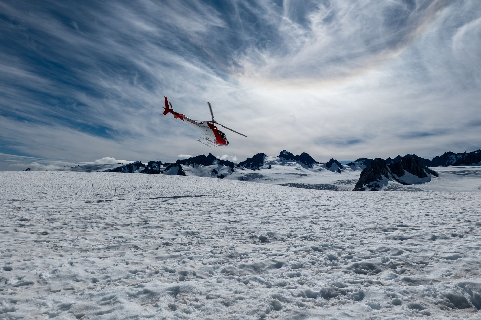 Helicopter flying over snowy Fox Glacier with stunning mountain backdrop in New Zealand.